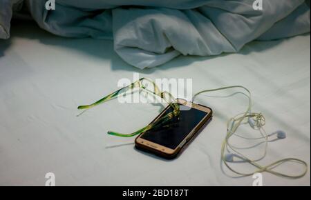 Auf dem Bett und mit einer Decke waren Handys und Kopfhörer platziert, er sah unordentlich aus, das Bett war zerknittert, nachdem ich spät am Tag aufwachte, nobod Stockfoto