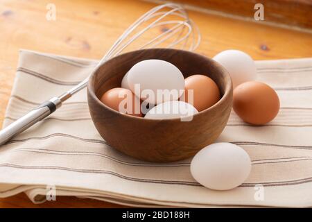 Rohe Eier in einer Holzschale und auf einem sauberen Tuch mit einem Mixer beiseite in warmem Licht und Holzhintergrund. Stockfoto