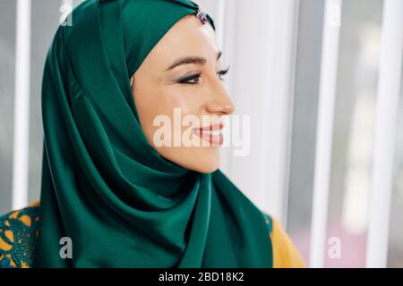 Schöne junge muslimische Frau in grünem Hijab lächelnd und wegblickend Stockfoto