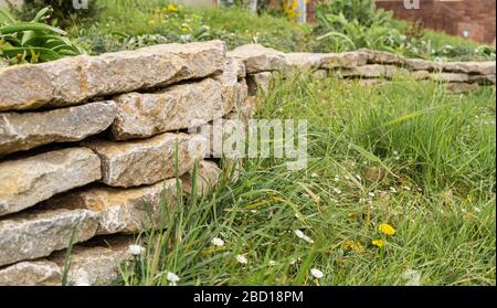 Mauer aus Steinen in einem Stadtpark. Stadtgärten. Eingezäunt von der Wiese. Haltewand. Stockfoto