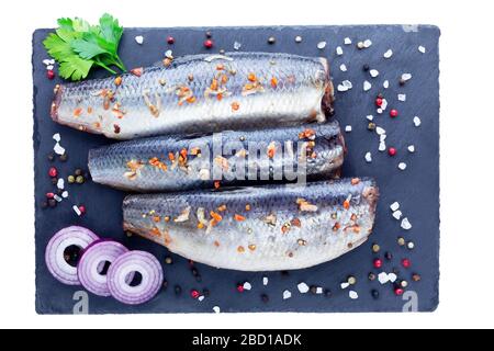 Salzter Hering mit Gewürzen, Zitronen- und roten Zwiebelringen isoliert auf weißem Grund. Marinierter Fisch in Scheiben. Draufsicht Stockfoto