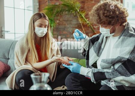 Frau und Mann, Paar in Schutzmasken und Handschuhen, isoliert zu Hause mit Coronavirus Atemsymptomen wie Fieber, Kopfschmerzen, Husten. Gesundheitswesen, Medizin, Quarantäne, Behandlungskonzept. Stockfoto