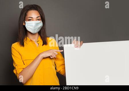 Schwarze Frau in medizinischer Maske zeigt auf leeren, leeren Banner-Signboard-Hintergrund Stockfoto