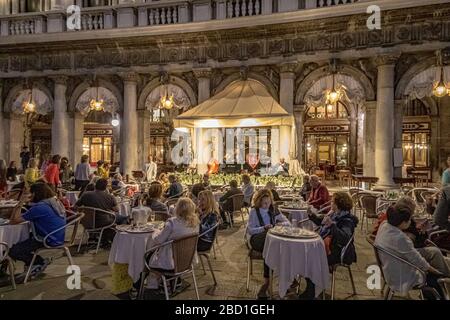 Leute, die draußen Caffè sitzen, sind Florian, ein berühmtes Café im Herzen des Markusplatzes, da die Band am frühen Abend in Venedig, Italien, spielt Stockfoto