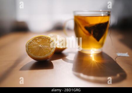 Schwarzer Tee mit Zitrone auf Holztisch. Teebeutel mit Zitronenscheibe im Becher Stockfoto