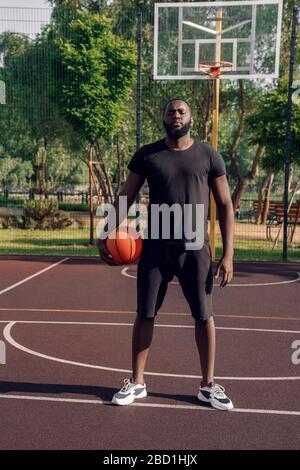 Aktivitäten Im Freien. Afrikanischer Mann steht mit Ball auf Basketballplatz posiert zuversichtlich Stockfoto