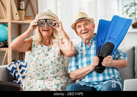 Ein älteres Paar sitzt im Reisebüro und trägt eine Schwimmmaske und Flossen und lacht fröhlich Stockfoto