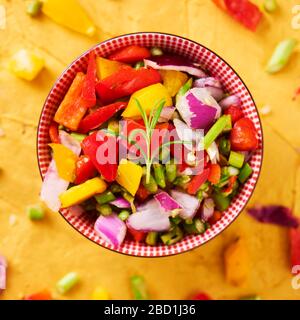 Hochwinkeliger Blick auf eine Schüssel mit einer Mischung verschiedener roher gehackter Gemüse, wie Spargel, Zwiebel oder gelber und roter Paprika, auf goldener Textur Stockfoto