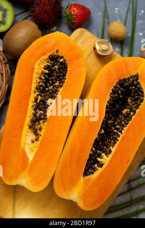 Papaya. Tropische Früchte. Nahaufnahme von zwei Hälften reifer Papaya mit Samen auf Holzschneidebrett. Papaya in Scheiben und andere exotische Früchte auf dem Tisch Stockfoto