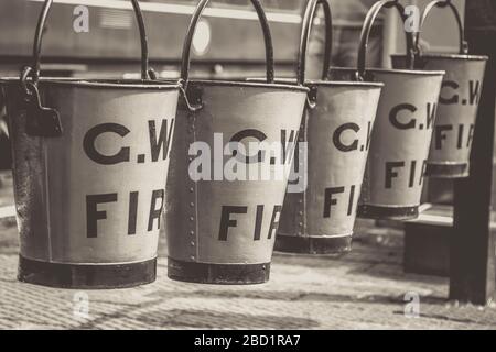 Mononahe Nahaufnahme von Vintage-Feuereimern, die in einer Reihe auf dem Bahnsteig des Vintage-Bahnhofs, der Severn Valley Dampfeisenbahn, hängen. Alte Löschanlagen. Stockfoto
