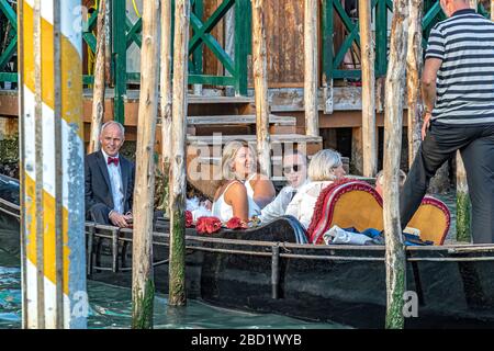 Eine Braut, die lächelt, wenn sie einen Gondolier anlächelt, während eine Hochzeitsgesellschaft eine Gondelfahrt entlang des Canal Grande in Venedig, Italien, unternimmt Stockfoto