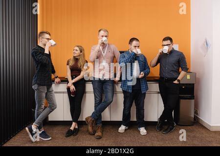 Fröhliche Kollegen haben Spaß an der Mittagspause im Büro, lächelnde multirassische Mitarbeiter lachen und trinken Kaffee. Stockfoto