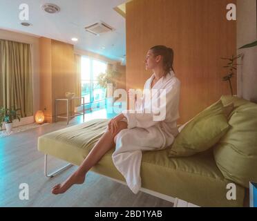 Junge hübsche Frau sitzt im weißen bademantel im entspannenden Spa-Raum im Nahbereich. Stockfoto