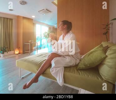 Junge hübsche Frau sitzt im weißen bademantel im entspannenden Spa-Raum im Nahbereich. Stockfoto