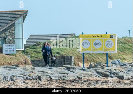 Garrettstown, West Cork, Irland. April 2020. Zwei Frauen gehen heute ihren Hund an einem Covid-19-Informationsschild am Garrettstown Beach vorbei. Kredit: Andy Gibson/Alamy Live News Stockfoto