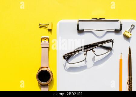 Home Office Arbeitsplatz Mockup mit Zwischenablage, Uhr, Brille und Zubehör. Checkliste, leeres Notizpapier auf gelbem Hintergrund. Büro, Schriftsteller oder Stockfoto