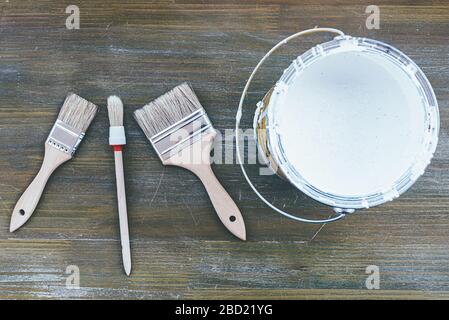 Draufsicht über verschiedene Lackbürsten und weiße Farbe auf Holzoberfläche, Heimverbesserungskonzept Stockfoto