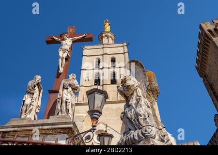 Dramatische Ansicht des Glockenturms der Kathedrale von Avignon, mit einem Statuenensemble der Kreuzigung im Vordergrund Stockfoto