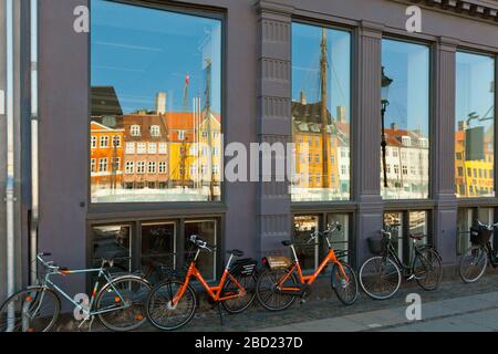 Fahrräder stehen vor einem Gebäude mit bunten historischen Häusern, die sich in den Fenstern spiegeln; Nyhavn, Kopenhagen Stockfoto