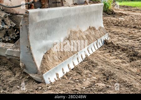 Der Bagger räumt das Grundstück für den Bau frei. Der Metalleimer des Baggers liegt auf dem Boden. Stockfoto