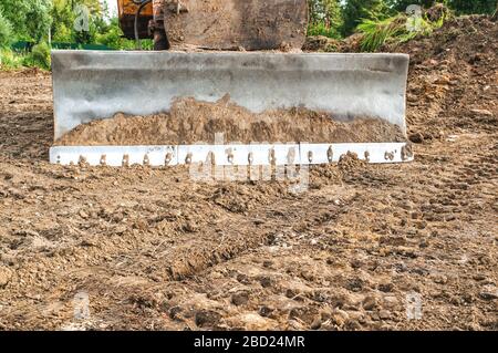 Der Bagger räumt das Grundstück für den Bau frei. Der Metalleimer des Baggers liegt auf dem Boden. Stockfoto