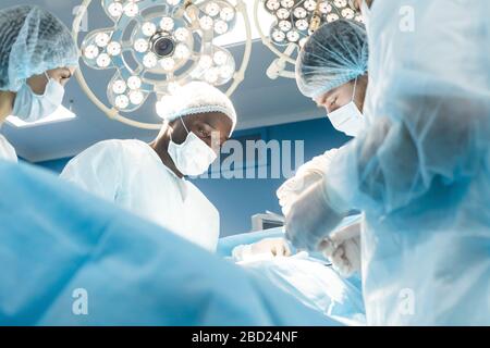 Ein internationales Ärzteteam führt eine komplexe chirurgische Operation an einem unter Anästhesie stehenden Patienten durch. Moderner Operationssaal und erfahrene Chirurgen Stockfoto