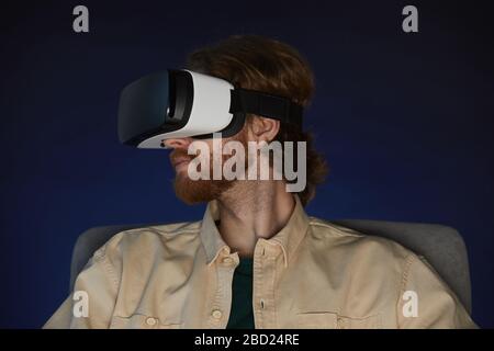 Seitenansicht Porträt des modernen bärtigen Mannes mit Virtual Reality Ausrüstung und mitreißendem Videospiel oder Film im Dunkeln Stockfoto