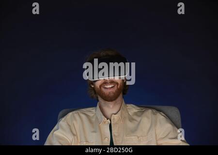 Kopf- und Schulterporträt erwachsener bärtiger Mann, der virtuelle Reality-Ausrüstung trägt, während er im Dunkeln immersives Videospiel oder Film genießt Stockfoto
