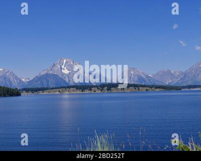 Mittlerer weiter Blick auf den Jackson Lake Dam mit den Grand Teton Bergketten im Hintergrund. Stockfoto
