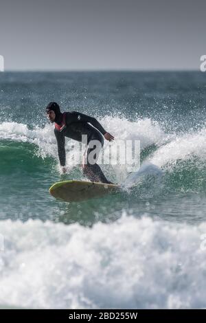 Ein Surfer, der ein Langbrett auf dem Kamm einer Welle verwendet, die nach rechts bei Fistral in Newquay in Cornwall bricht. Stockfoto