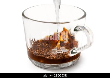 Gießen Sie warmes Wasser in den auf Weiß isolierten Gras-Becher auf sofortigen Kaffee. Teilweise aufgelöster Kaffee. Stockfoto