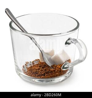 Trockener Instantkaffee und Zuckerwürfel in einem Glasbecher mit Metalllöffel, isoliert auf Weiß. Stockfoto