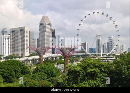 Das Singapore Flyer Ferris Rad dominiert die Landschaft in den Gärten an der Bucht mit den Stadttürmen, die die Kulisse bieten. Stockfoto