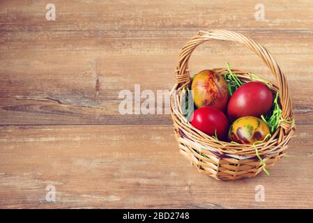 Easter Weidenkorb mit farbigen Eiern auf braunem Holzbrett. Stockfoto