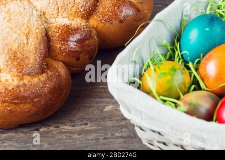 Osternkorb mit bunten Eiern und Osterbrot auf grauem Holzbrett. Stockfoto
