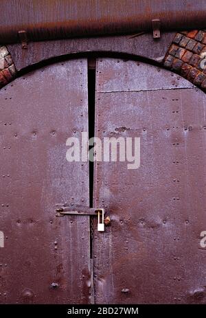 Architektur. Eisenbahnbogen aus viktorianischem Backstein. Rostige, mit einem Vorhängeschloss verschlossene Tür. Stockfoto