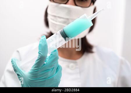 Eine Krankenschwester, die eine Maske und Handschuhe trägt, die eine Spritze mit Virusimpfstoff in einer modernen Klinik hält Stockfoto