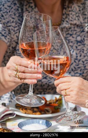 Hände von zwei Frauen, die mit einer Brille Rosengwein toasten. Stockfoto