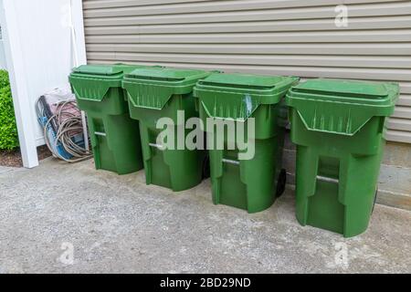 Der horizontale Schuss aus vier grünen Kunststoff-Abfallbehältern verläuft gegen die Außenwand einer Eigentumswohnung. Stockfoto