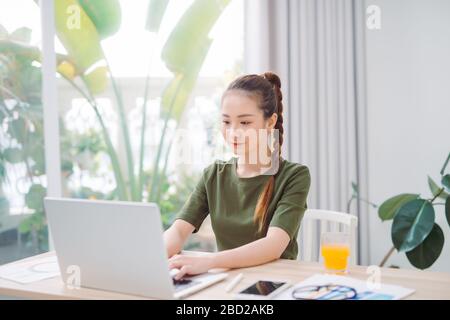Hübsche asiatische Frau, die E-Mails auf dem Laptop tippt, während sie zu Hause sitzt Stockfoto