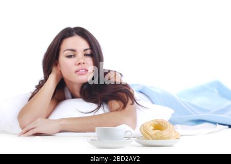 Frau, die einen Donut isst und im Bett Kaffee trinkt, isoliert auf weißem Hintergrund Stockfoto