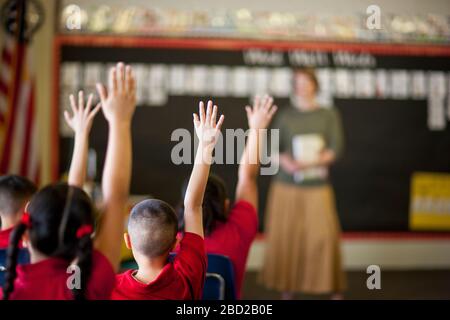 Schüler mit erhobenen Händen in einem Klassenzimmer. Stockfoto