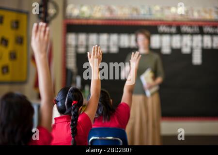 Schüler mit erhobenen Händen in einem Klassenzimmer. Stockfoto