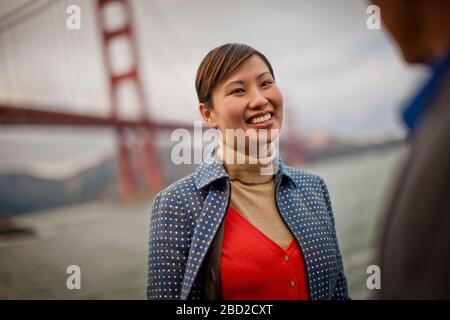 Lächelnde junge Frau spricht mit einem Freund von der Golden Gate Bridge in San Francisco, USA. Stockfoto
