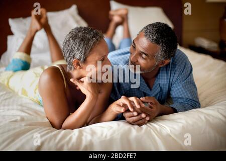 Reifes Paar, das die Hände hält und auf dem Bett liegt Stockfoto