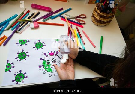 Ein Kind Färbung Virus Malerei auf einem Tisch voller Farben und eine Flasche hydroalkoholisches Gel Stockfoto