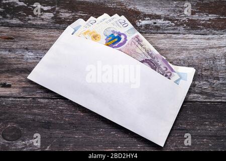 Britische Banknoten in einem weißen Umschlag auf einem Holztisch. Stockfoto