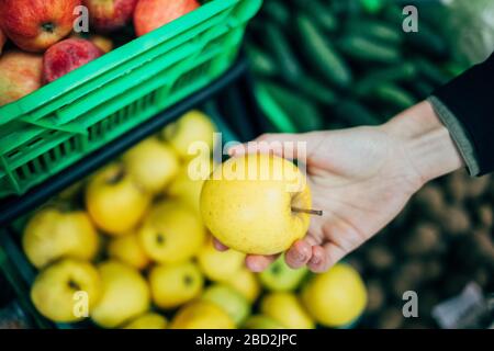 Weibliche Hand, die apfel aus dem Regal im Lebensmittelgeschäft pflückt, Nahaufnahme. Stockfoto