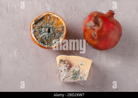 Verdorbene faule Speisen mit Schimmel: Halbe Orange, Granatapfel und Hartkäse auf grauem Hintergrund, Draufsicht Stockfoto