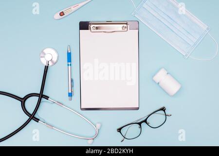 Medizinisches Mock-up mit leerem Blatt Papier in der Zwischenablage und Stethoskop, medizinischer Maske und anderen Arztwerkzeugen, Stockfoto